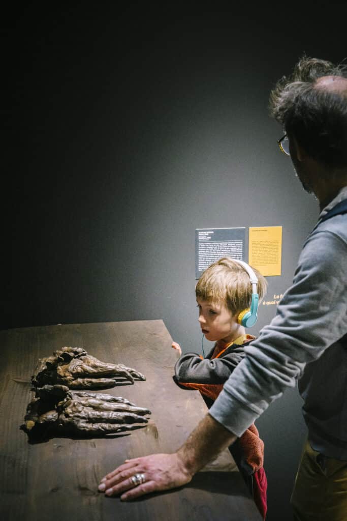 Garçon écoutant une histoire avec Lunii devant une oeuvre de l'exposition Le Chant des Forêts