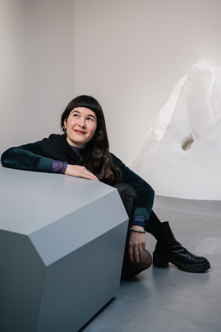 Portrait de l'artiste Justine Bougerol devant son oeuvre dans l’exposition CHAOSMOS au MAIF Social Club, invitation faite à 12 artistes de nous raconter le cosmos et d’inventer de nouvelles manières d’habiter la Terre, par la commissaire Jos Auzende et scénographiée par Lucie Gautrain, à Paris.