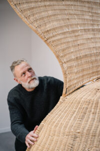Portrait de l'artiste Porky Hefer devant son oeuvre dans l’exposition CHAOSMOS au MAIF Social Club, invitation faite à 12 artistes de nous raconter le cosmos et d’inventer de nouvelles manières d’habiter la Terre, par la commissaire Jos Auzende et scénographiée par Lucie Gautrain, à Paris.