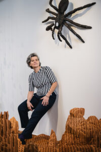 Portrait de l'artiste Virginie Yassef devant son oeuvre dans l’exposition CHAOSMOS au MAIF Social Club, invitation faite à 12 artistes de nous raconter le cosmos et d’inventer de nouvelles manières d’habiter la Terre, par la commissaire Jos Auzende et scénographiée par Lucie Gautrain, à Paris.