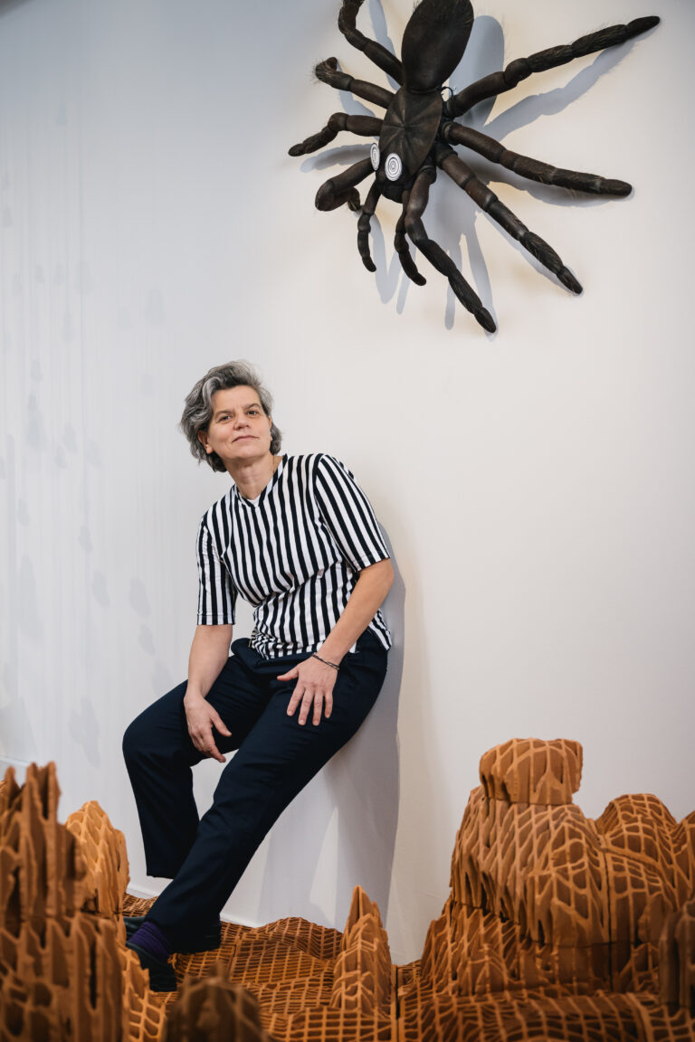 Portrait de l'artiste Virginie Yassef devant son oeuvre dans l’exposition CHAOSMOS au MAIF Social Club, invitation faite à 12 artistes de nous raconter le cosmos et d’inventer de nouvelles manières d’habiter la Terre, par la commissaire Jos Auzende et scénographiée par Lucie Gautrain, à Paris.